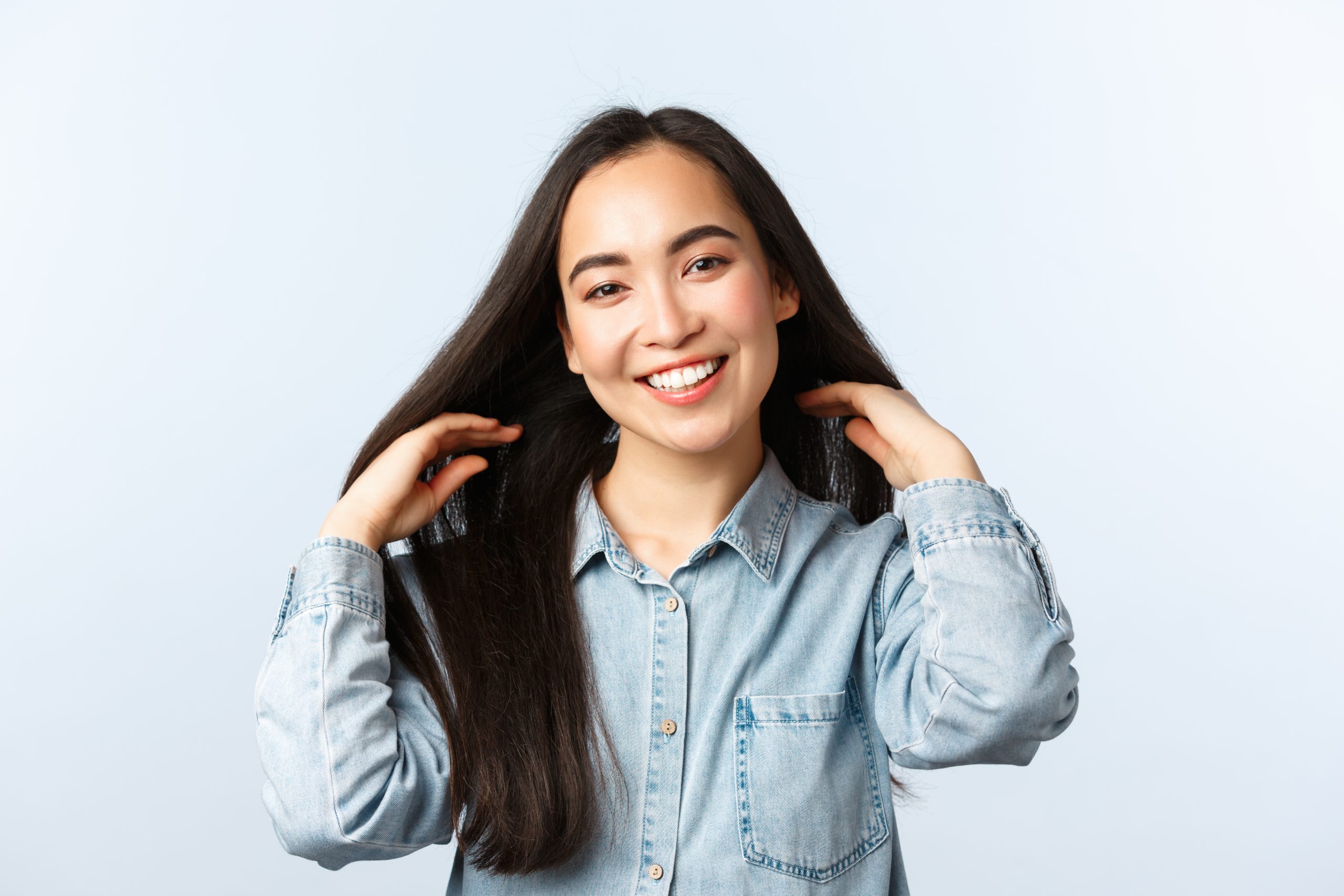 Lifestyle, people emotions and beauty concept. Attractive dreamy asian girl smiling and touching long straight dark hair, trying new hair products, visit hairdresser or beauty salon