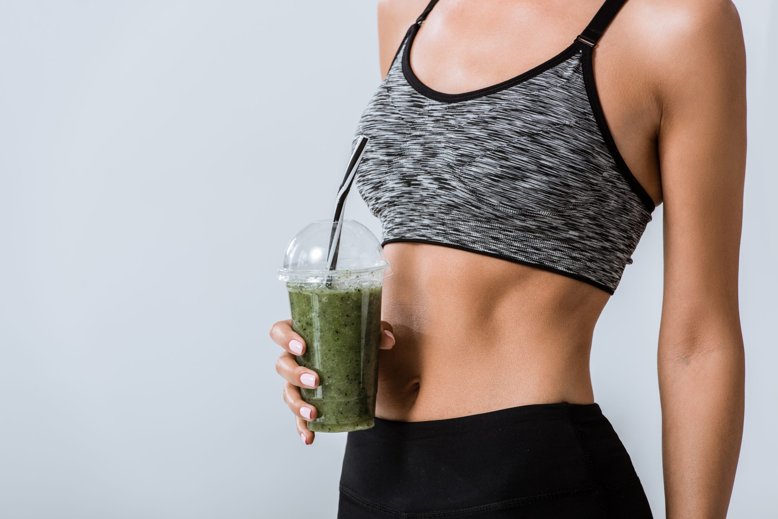 partial view of sportswoman holding smoothie isolated on grey